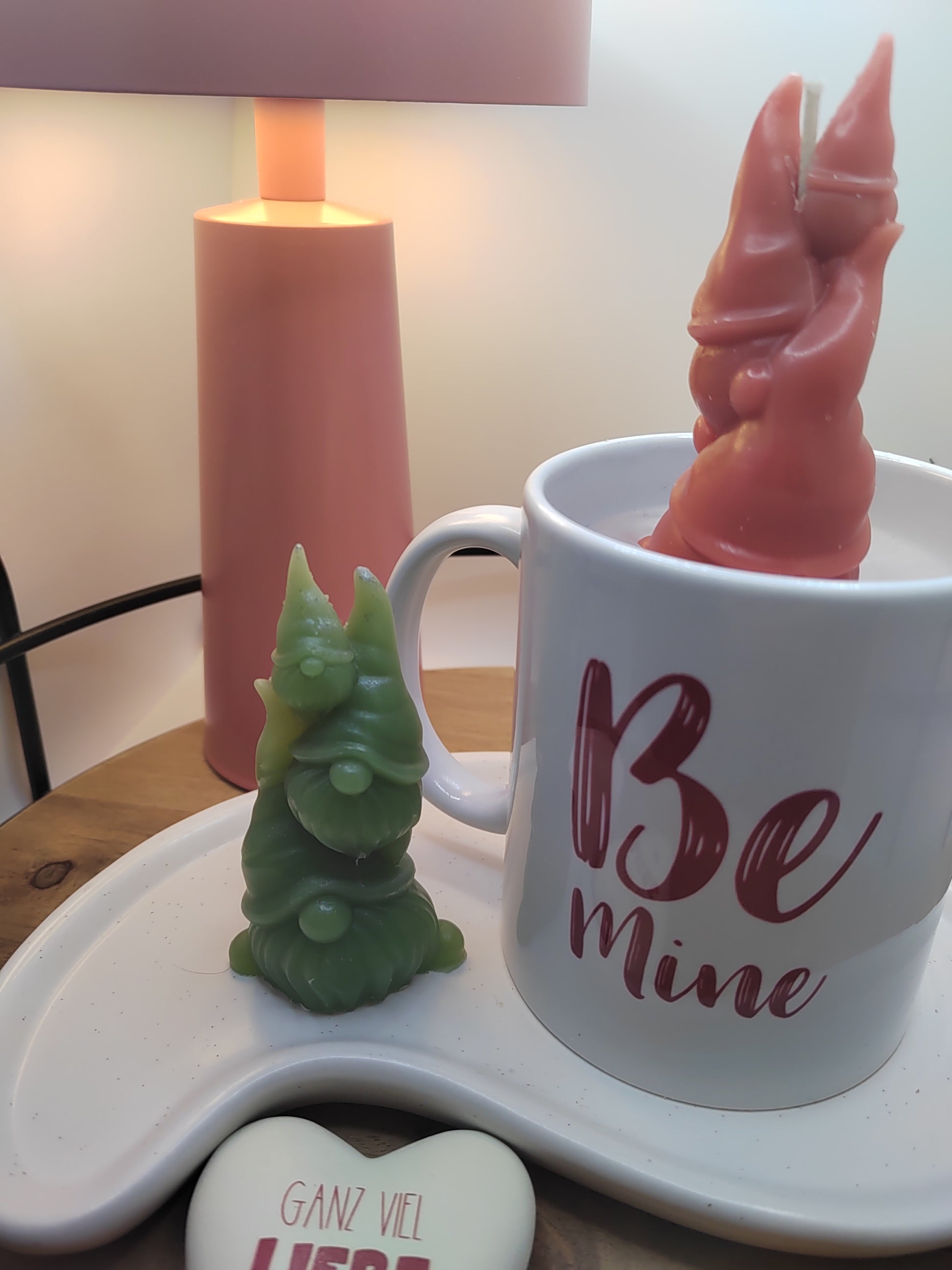 „Be Mine“-Kerze mit roter Wichtelfamilie in der Tasse und grüner Wachsfigur daneben