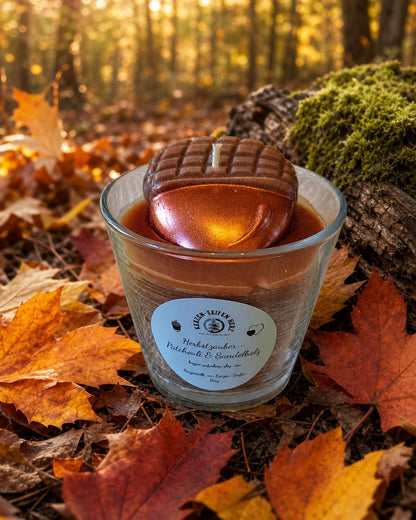 Brennende Herbstzauber-Duftkerze zwischen orangefarbenem Herbstlaub und Eichel-Dekoration