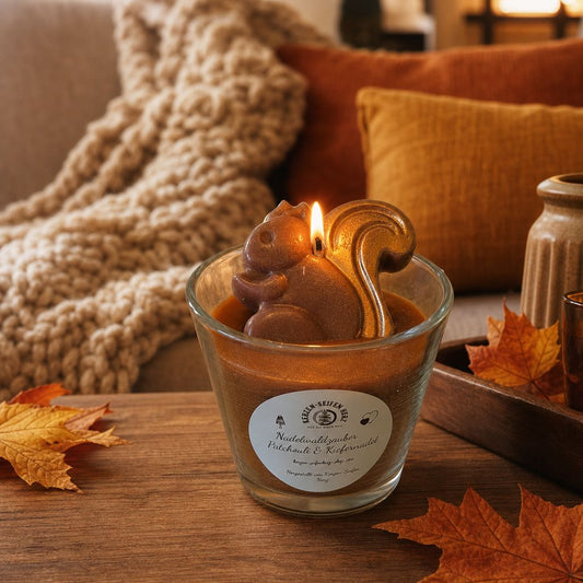 Brennende Nadelwaldzauber-Duftkerze im Glas mit Eichhörnchen-Dekoration auf Holztisch mit Strickdecke und Herbstlaub