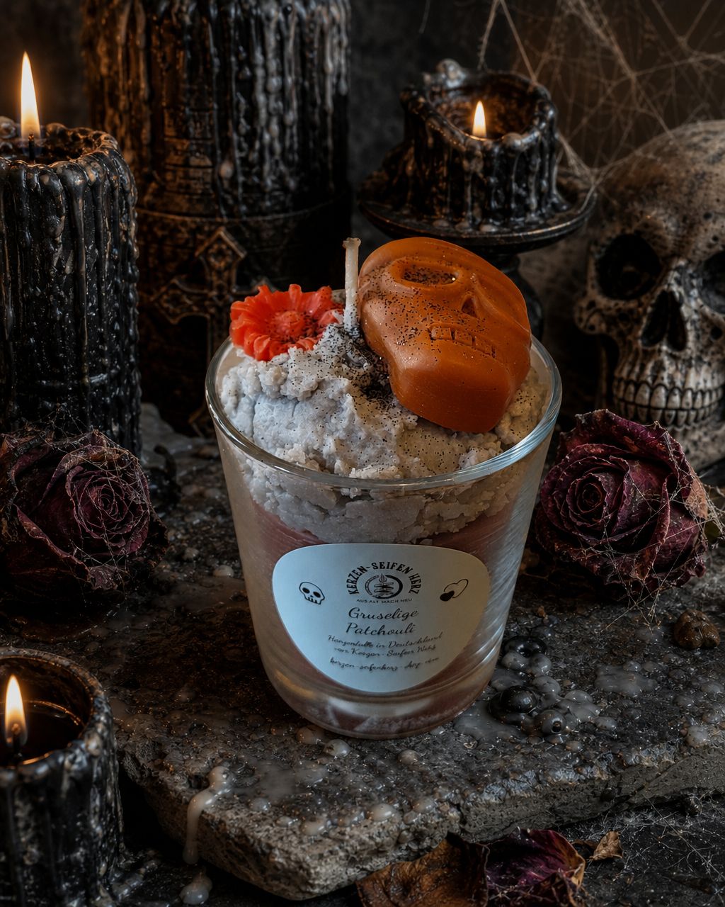 Gothic-Duftkerze im Glas mit orangefarbenem Totenkopf auf dunkler dekorativer Unterlage