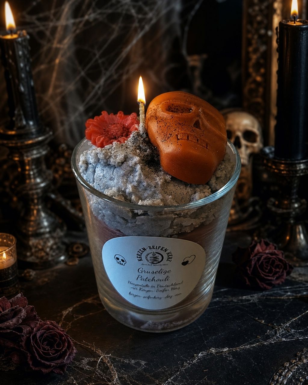 Brennende Patchouli-Duftkerze im Glas mit orangefarbenem Totenkopf und Blüte in dunkler Gothic-Atmosphäre