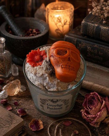 Nahaufnahme der „Gruseliger Patchouli“-Kerze mit Totenkopf, Blüte und mystischer Dekoration