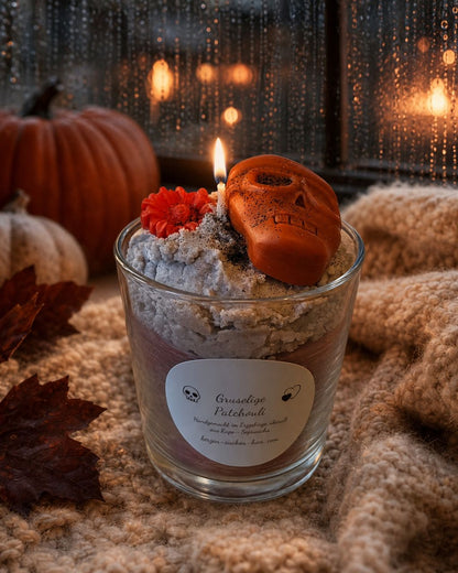 Patchouli-Duftkerze mit orangefarbenem Totenkopf zwischen Kürbissen und gemütlicher Herbstdekoration