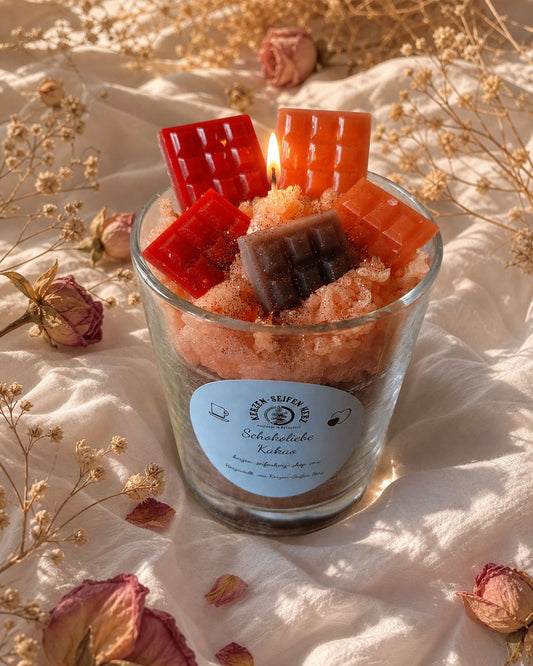 Schokoliebe-Duftkerze im Glas mit roten, orangefarbenen und dunklen Mini-Schokoladentafeln auf hellem Stoff