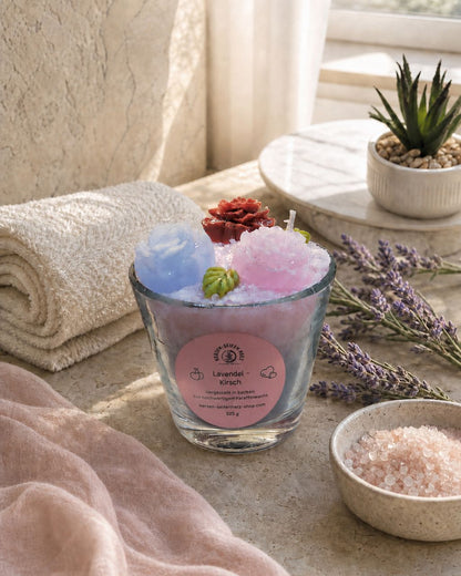 Lavendel-Kirsch Duftkerze im Wellness-Ambiente mit Handtuch, Lavendelzweigen und rosa Badesalz