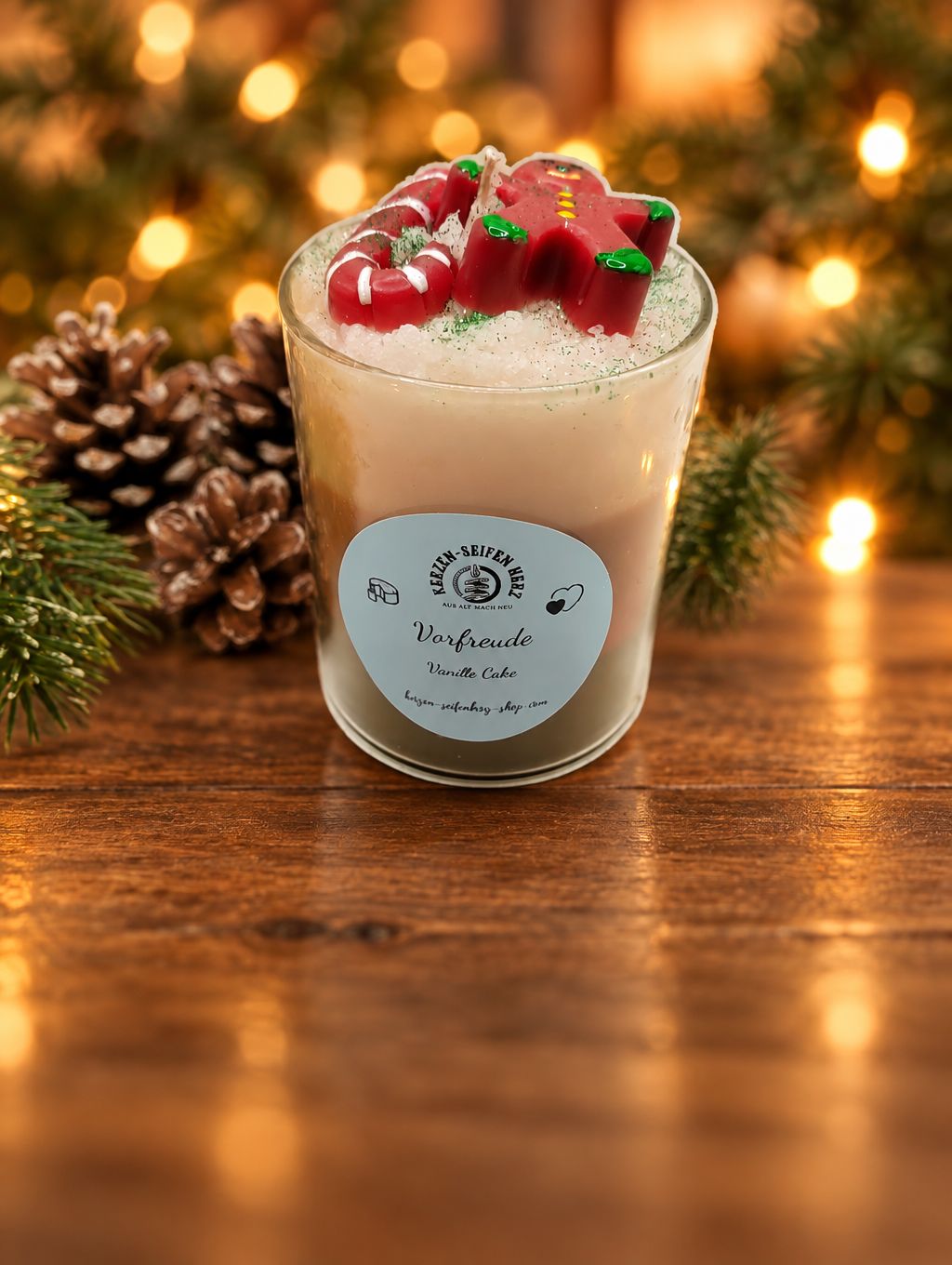 Weihnachtskerze im Glas „Vorfreude – Vanille Cake“ mit Lebkuchenfigur und Zuckerstange vor festlichem Lichterhintergrund