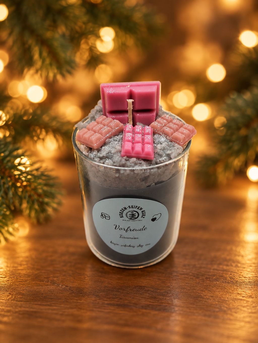 Weihnachtskerze im Glas „Vorfreude – Tiramisu“ mit rosa Schokoladendekor vor goldenem Lichterhintergrund