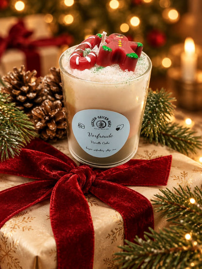 Vanillecake-Weihnachtskerze im Glas mit Lebkuchenmännchen und Zuckerstange auf weihnachtlich verpacktem Geschenk