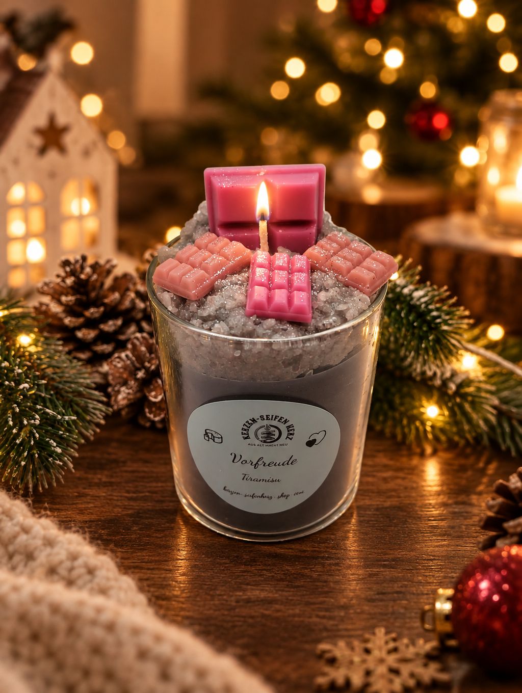 Tiramisu-Weihnachtskerze im Glas mit rosa Schokoladendekoration auf kuscheliger Decke und festlicher Beleuchtung