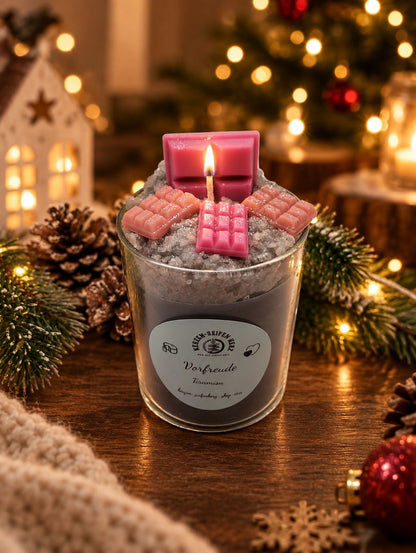Tiramisu-Weihnachtskerze im Glas mit rosa Schokoladendekoration auf kuscheliger Decke und festlicher Beleuchtung