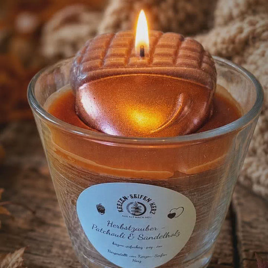 Herbstzauber-Duftkerze mit Flamme zwischen natürlichen Herbstmaterialien und gemütlicher Dekoration